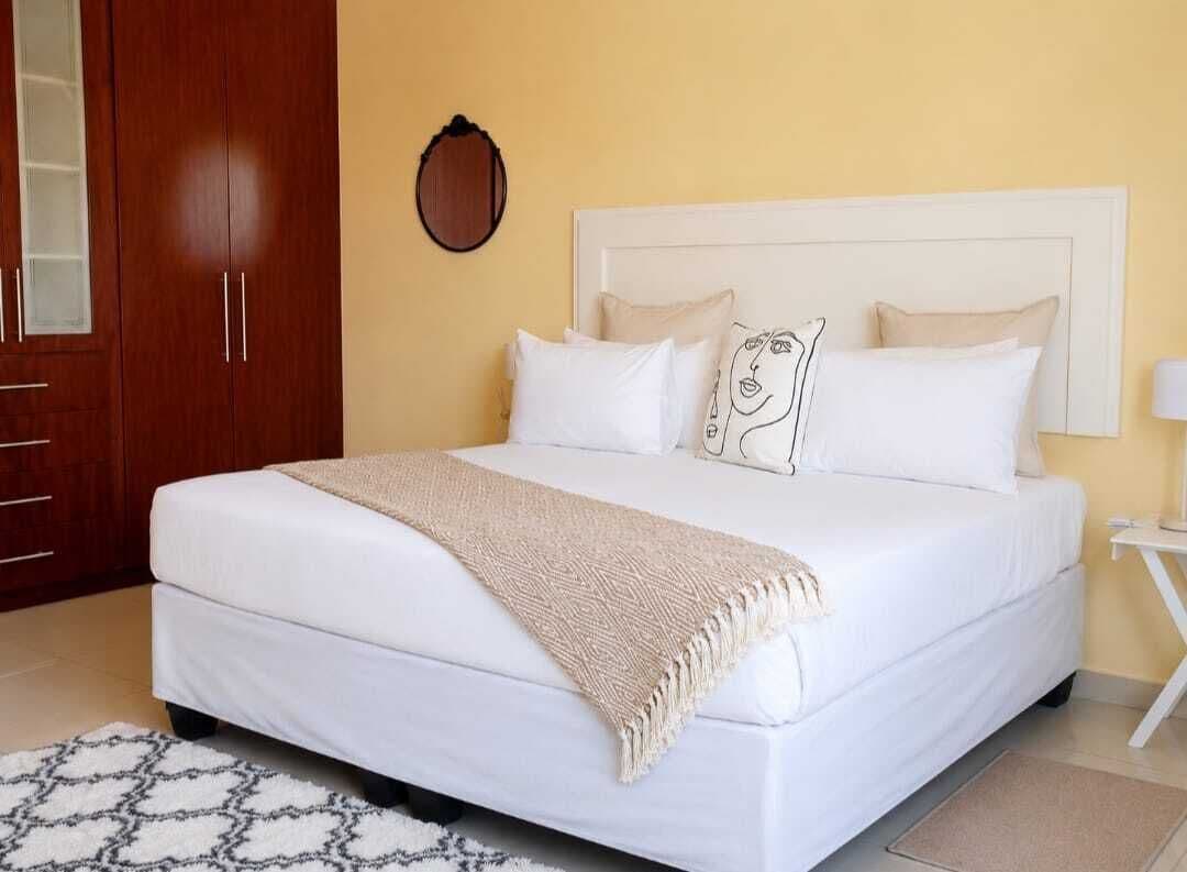 Una cama con ropa de cama blanca, un edredón color beige y almohadas estampadas.