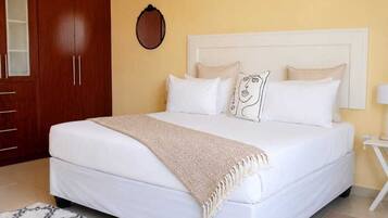 Una cama con ropa de cama blanca, un edredón color beige y almohadas estampadas.