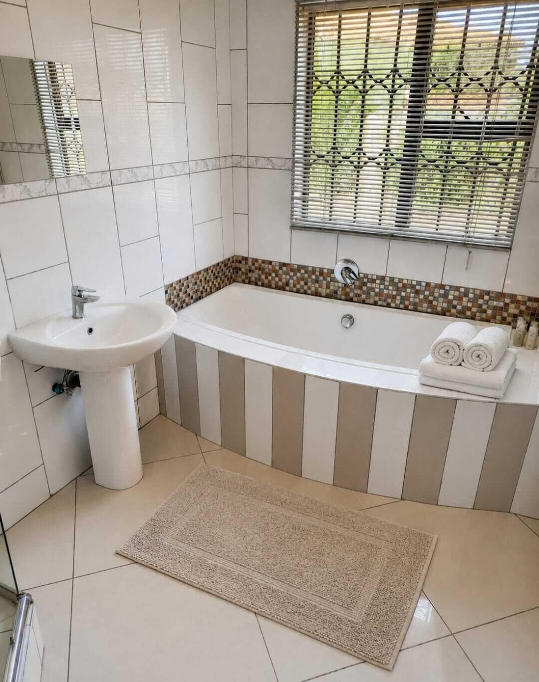 A bathroom with a sink, bathtub, and window with blinds.