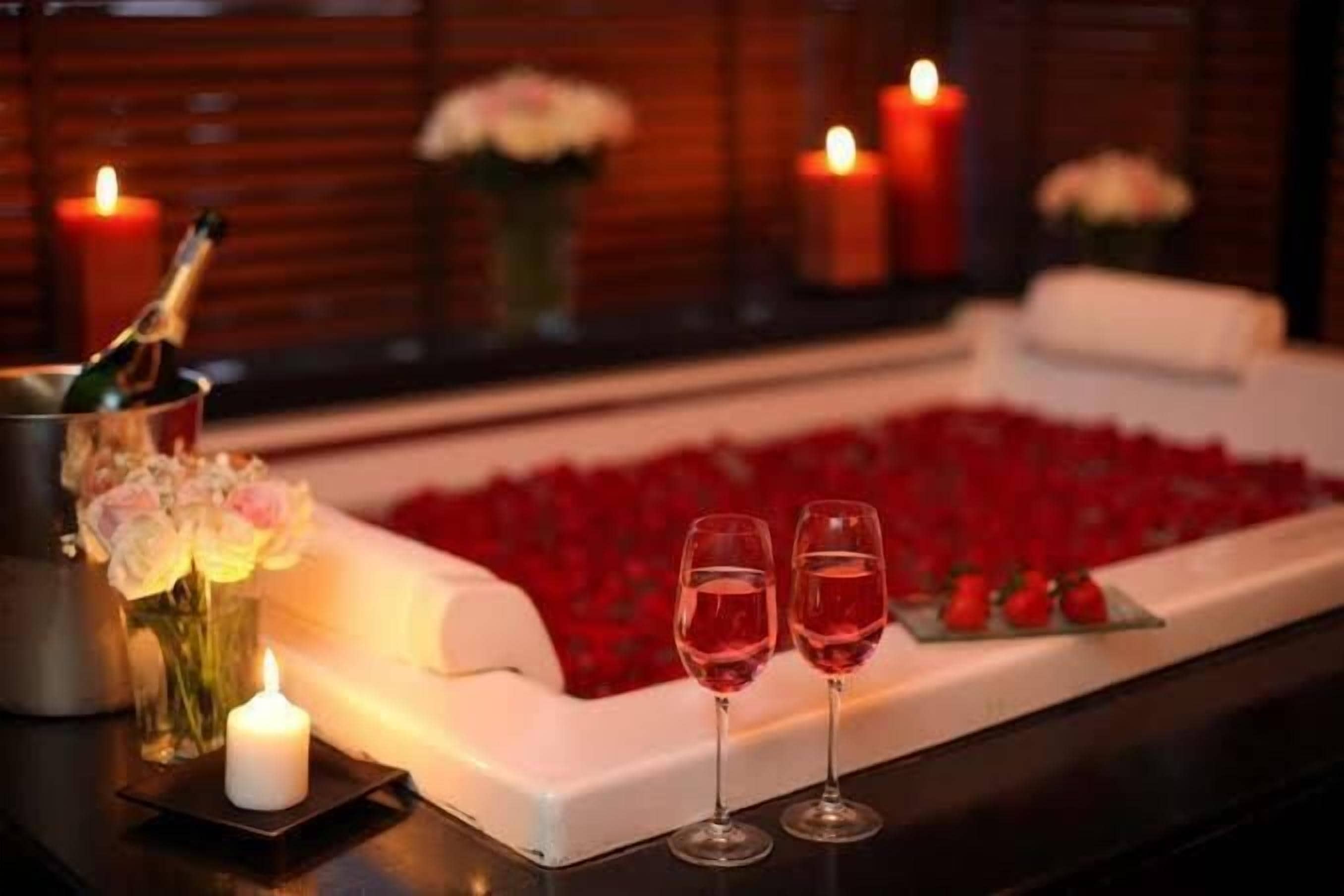 Romantisk stemning med en champagneflaske, to glas rødvin og en blomsterdekoration på et bord.