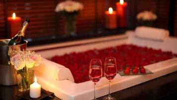 Romantisk stemning med en champagneflaske, to glas rødvin og en blomsterdekoration på et bord.