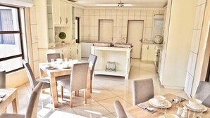 Une cuisine moderne avec des meubles blancs, un îlot central et un coin repas comprenant des chaises et des tables dressées pour le repas.