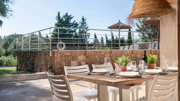 An outdoor dining area with a stone wall, white chairs, and a table set for a meal. - Alcudia's Best: Private Pool, BBQ, Inviting Garden (Alcúdia)