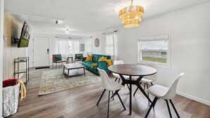 Uma sala de estar moderna com área de jantar, um sofá, uma mesa de centro e um candelabro.