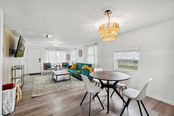 A modern living room with a dining area, a sofa, a coffee table, and a chandelier.