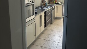 A kitchen with a gas stove, oven, and refrigerator. There is a window providing natural light and a view of trees outside. - Apartment beziers (Béziers)