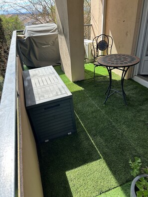 A patio with artificial grass, a covered grill, a table with a mosaic top, and a chair. - Apartment beziers (Béziers)