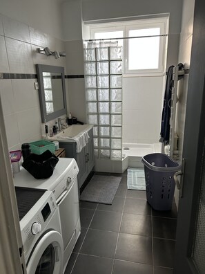 A compact bathroom with a washing machine, a sink, a mirror, a shower area, and a window. - Apartment beziers (Béziers)
