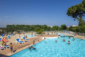 Une piscine dotée de plusieurs couloirs et d’une zone peu profonde réservée aux enfants, entourée de chaises longues et agrémentée d’une pergola en bois.