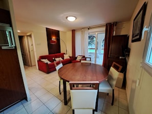 Un comedor con una mesa redonda de madera y sillas blancas, un sofá rojo e iluminación en el techo.