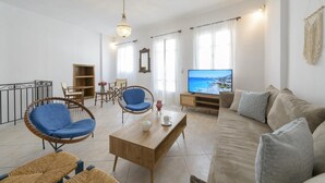 A living room with a sofa, two blue chairs, a wooden coffee table, a TV, and a view of the sea. - Rethymno Heart Apartment (Rethymno)