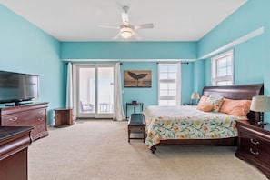 A bedroom with a bed, a TV, a ceiling fan, and a window with curtains.