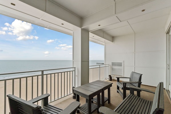 A balcony with a view of the ocean, furnished with wooden chairs and tables.
