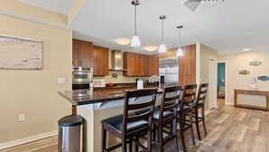 A modern kitchen with wooden cabinets, stainless steel appliances, and a central island with bar stools. - Book Mermaid's Lookout 410B | Sandbridge Oceanfront Rental (Virginia Beach)