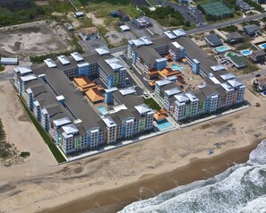 A coastal hotel with multiple buildings, a beach, and a swimming pool.