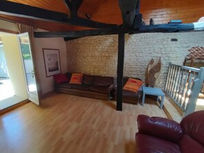 Ein Wohnzimmer mit Steinwand, Holzbalken, einer Couch und einem roten Ledersessel.