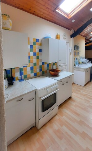 Cozinha com painel de azulejos, armários brancos, fogão e teto de madeira.