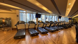 Ein Fitnessraum mit Laufbändern an der Wand, großen Fenstern und einem Holzboden.