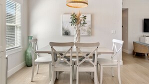 A dining area with a white table and chairs, a woven pendant light, and a framed picture on the wall. - Heaven At The Sound: Fully Remodeled | Dogs OK (Kill Devil Hills)