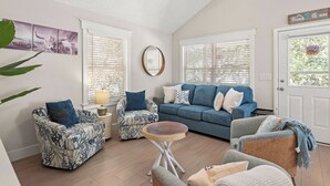 A cozy living room with a blue sofa, patterned armchairs, and a round wooden table. - Heaven At The Sound: Fully Remodeled | Dogs OK (Kill Devil Hills)