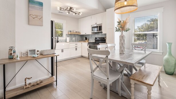 A modern kitchen with white cabinets, a wooden dining table, and a hanging light fixture. - Heaven At The Sound: Fully Remodeled | Dogs OK (Kill Devil Hills)
