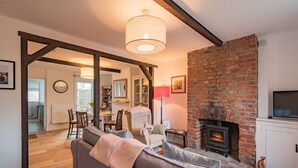 A cozy living room with a fireplace, a sofa, a dining area, and a kitchen in the background. - Bunny Cottage by Bloom Stays -  sleeps 4 guests  in 2 bedrooms (Saltwood)