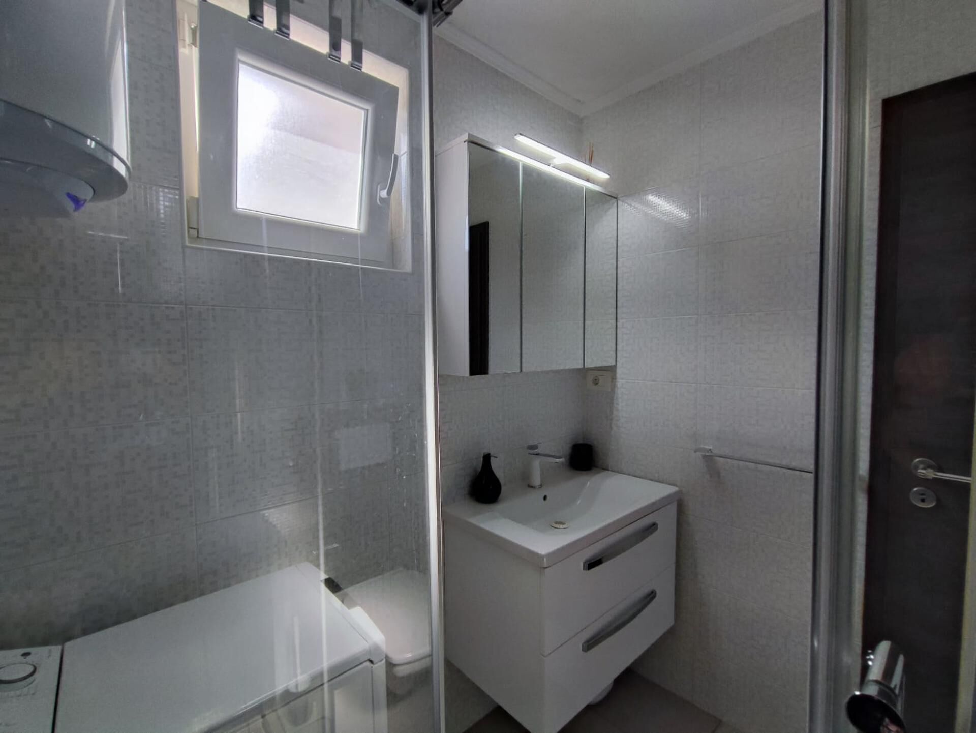 Een moderne badkamer met een glazen douchecabine, een witte wastafel en een spiegel.