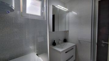 Een moderne badkamer met een glazen douchecabine, een witte wastafel en een spiegel.