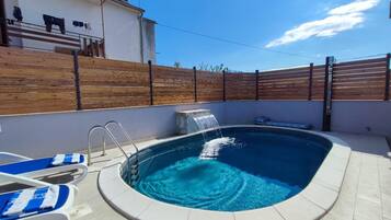 Una piscina con cerramiento de madera, una fuente de agua y sillas de descanso.