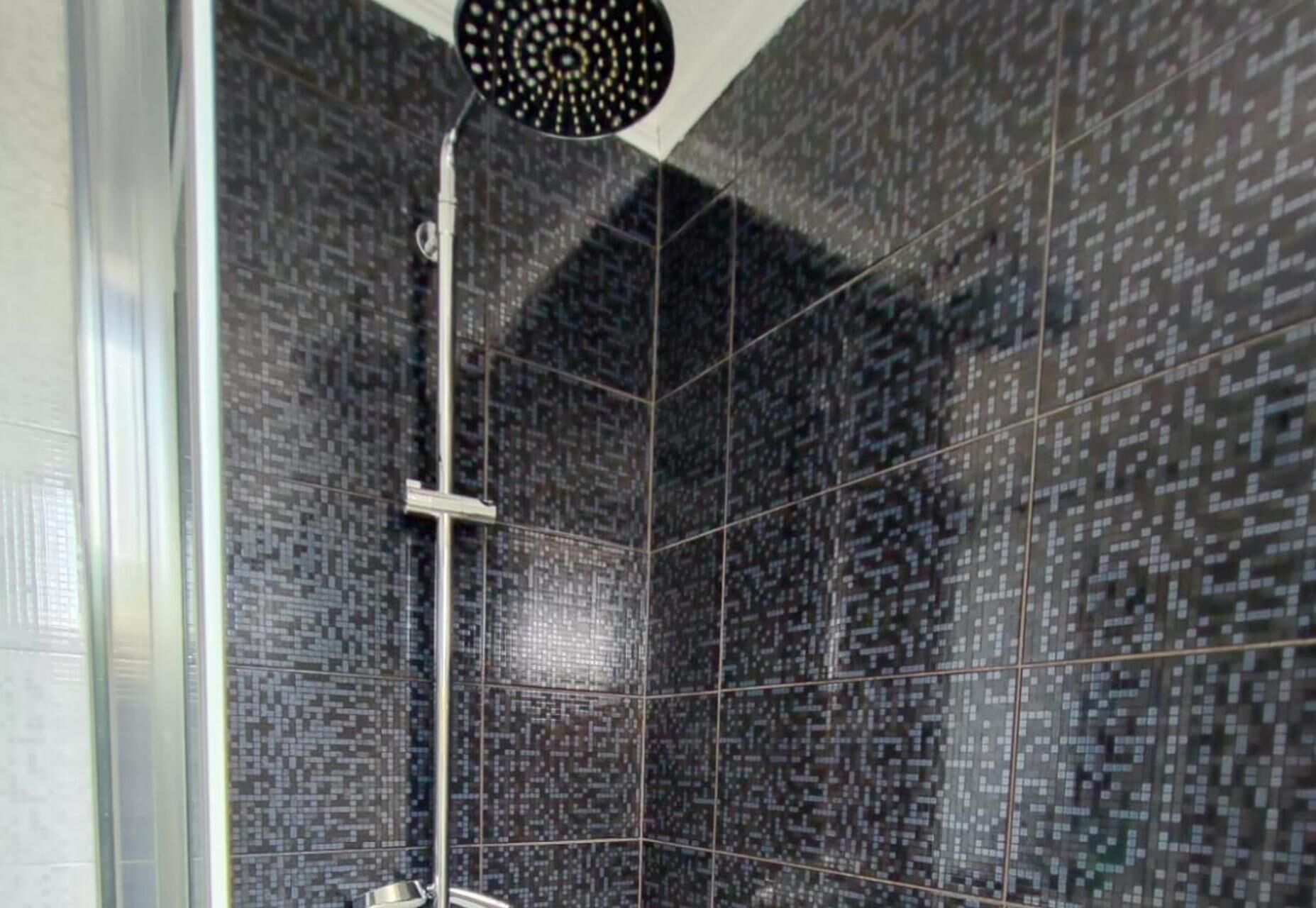 A shower with a modern design, featuring a patterned tile wall and a ceiling-mounted showerhead.