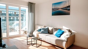 Un salon moderne avec un canapé, une table basse et une grande fenêtre donnant sur un immeuble.