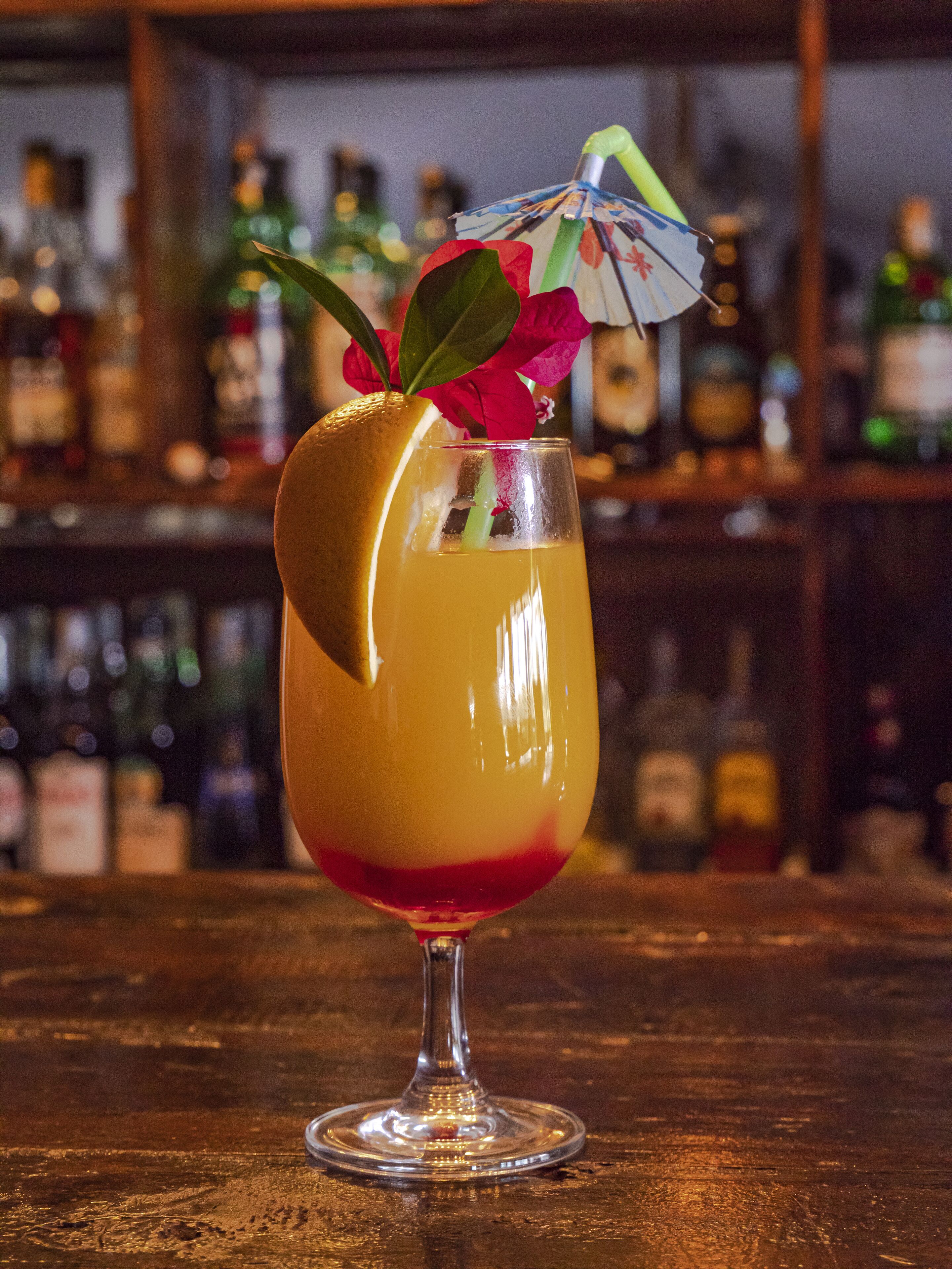 A cocktail in a glass with a decorative umbrella and flower garnish.