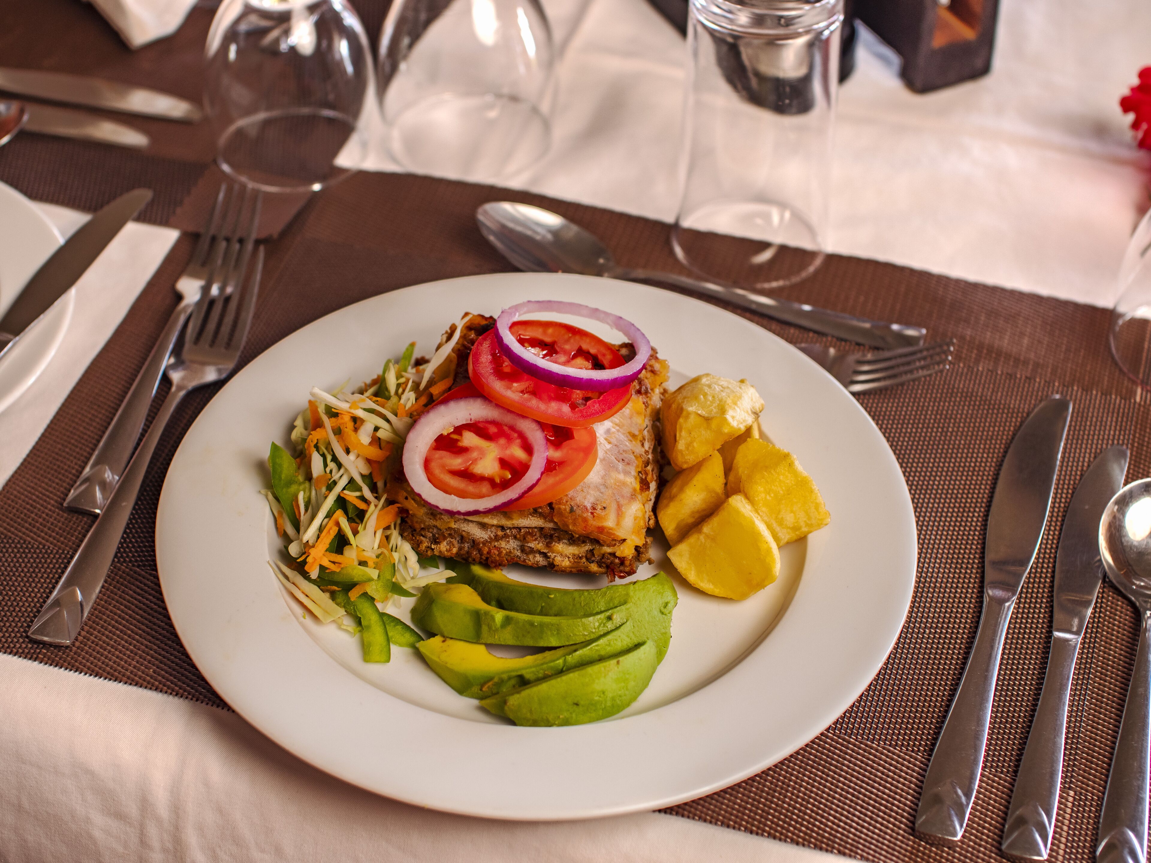 Un plato de comida con aguacate, tomate, cebolla y una ensalada sobre un plato blanco.