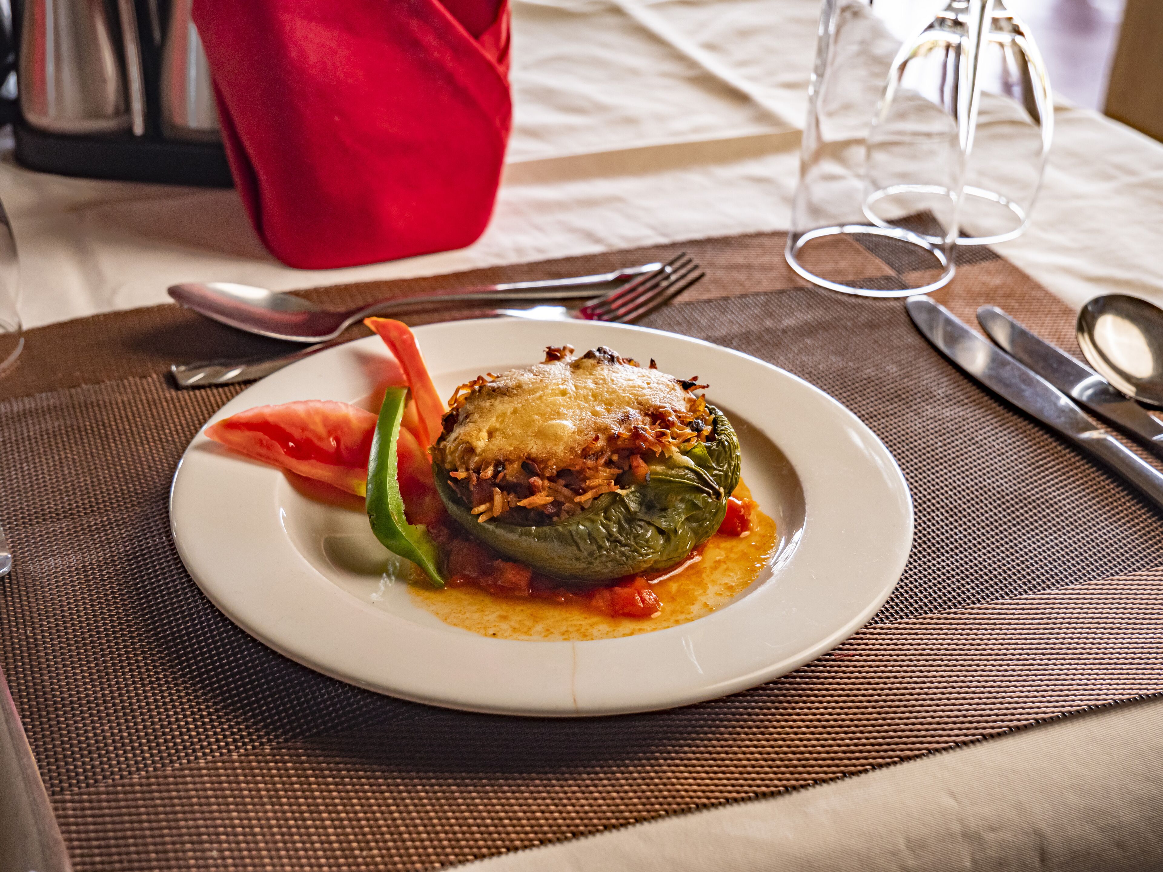 A plate with a stuffed pepper, a fork, a knife, and a glass on a table with a placemat.