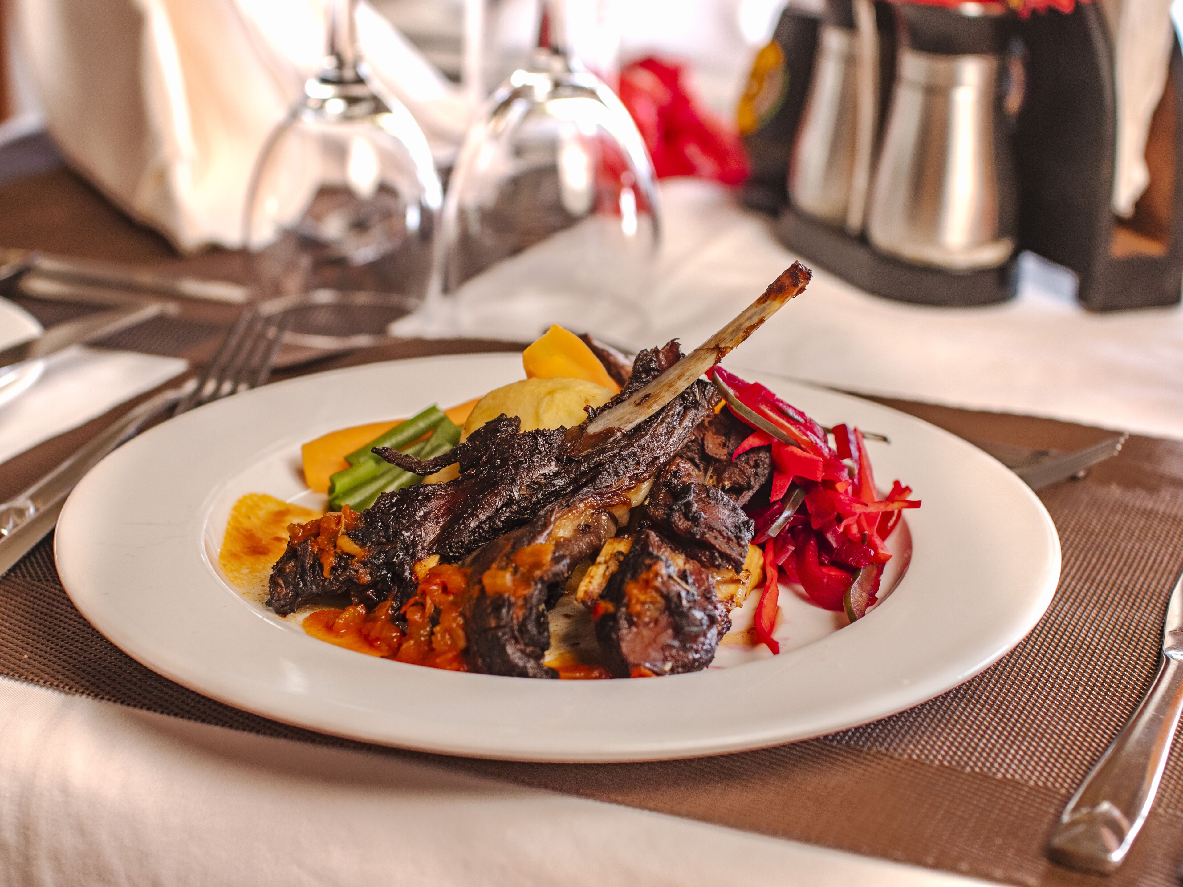 A plate of food with a lamb shank, vegetables, and a sauce.