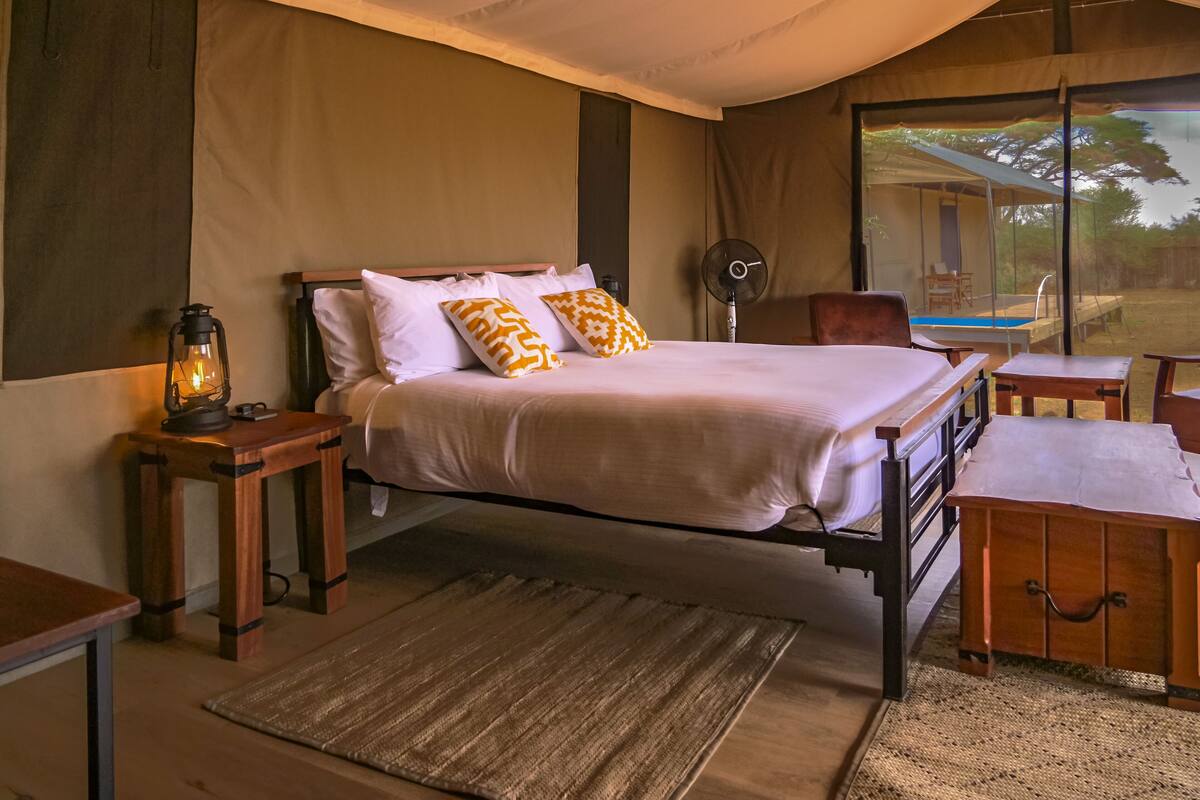 A bedroom with a bed, bedside tables, a fan, and a view of the outdoors.