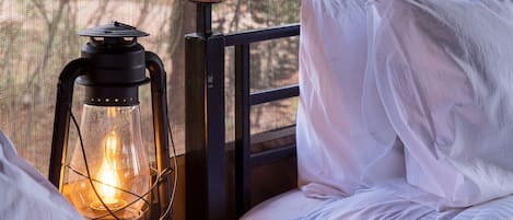 A bed with white bedding, a wooden nightstand, a lantern, and a power outlet.