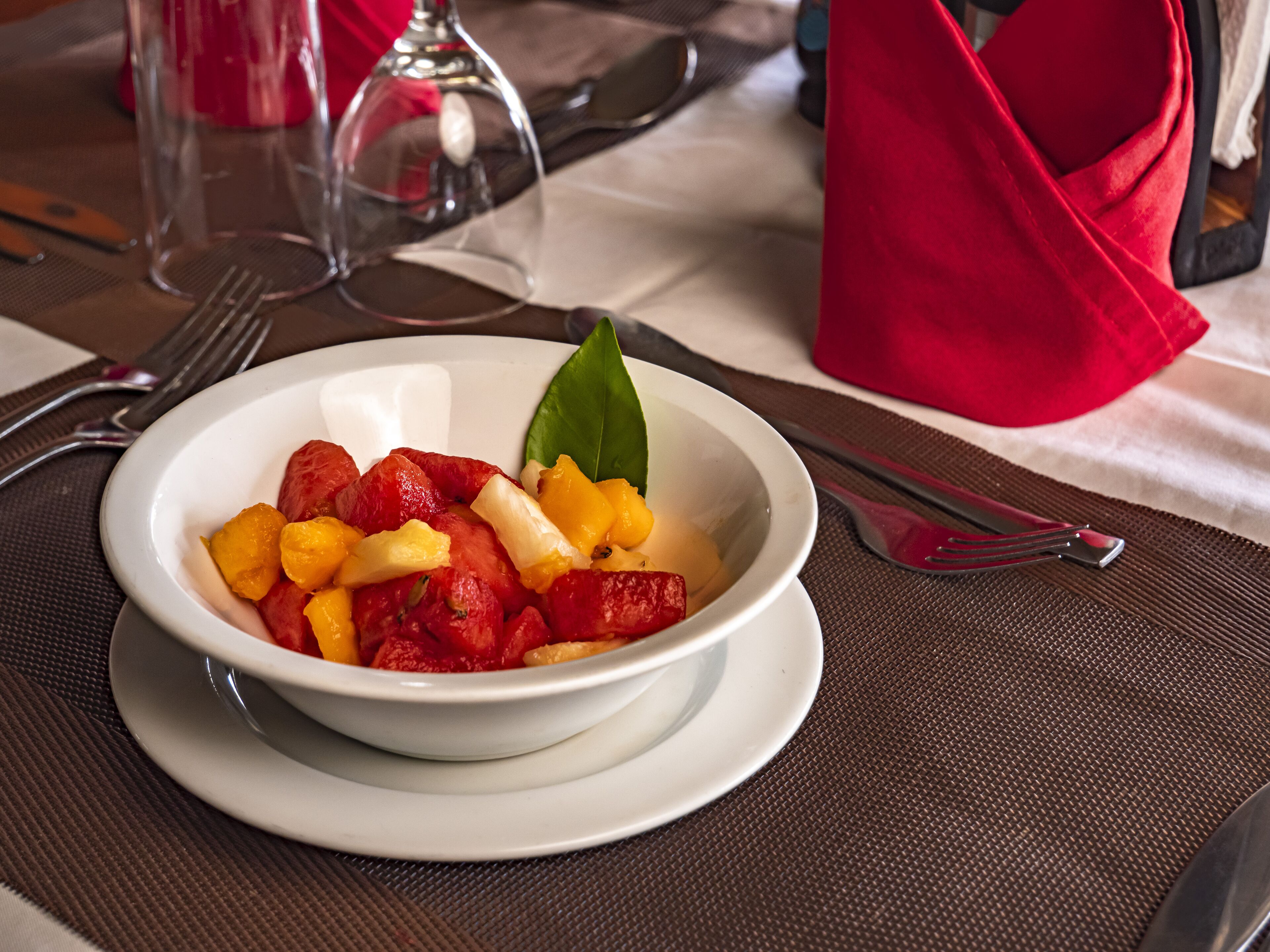 Ensalada de frutas en un tazón sobre un plato blanco, con un camino de mesa marrón debajo.