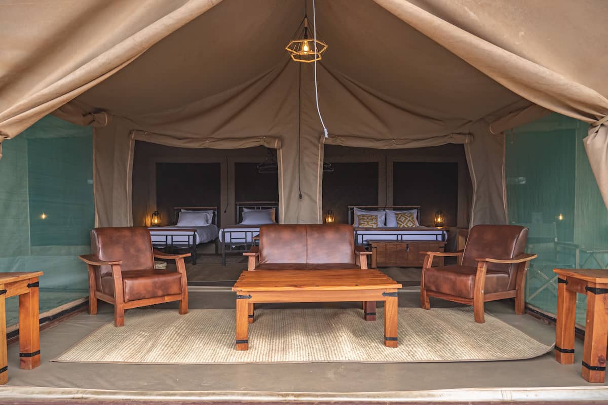 A tented accommodation with two beds, a sofa, and wooden furniture.