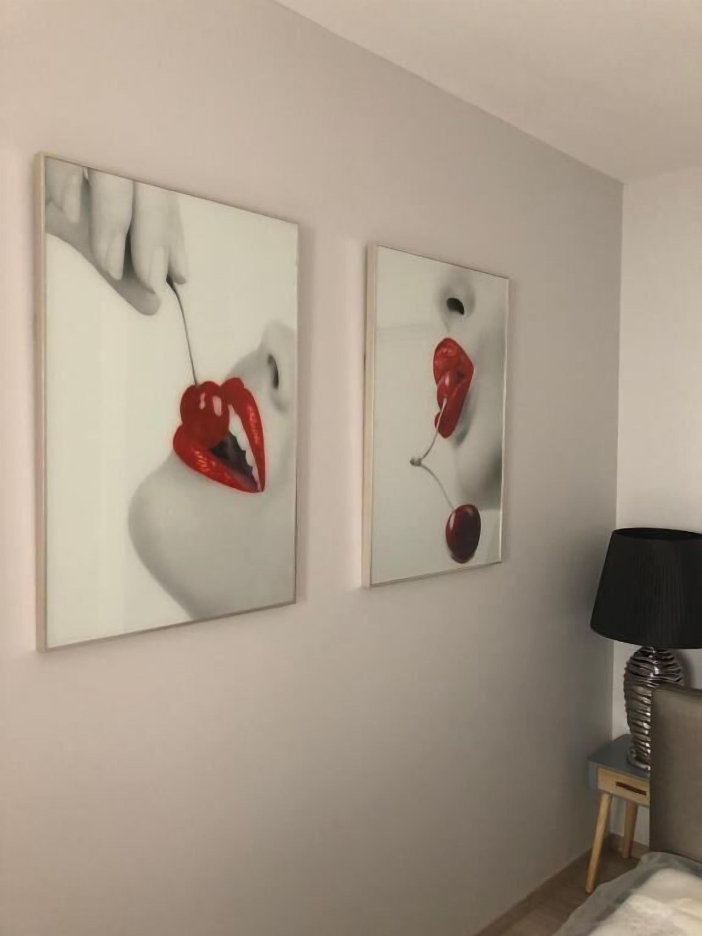 Duas pinturas abstratas numa parede, uma luminária e uma cama.