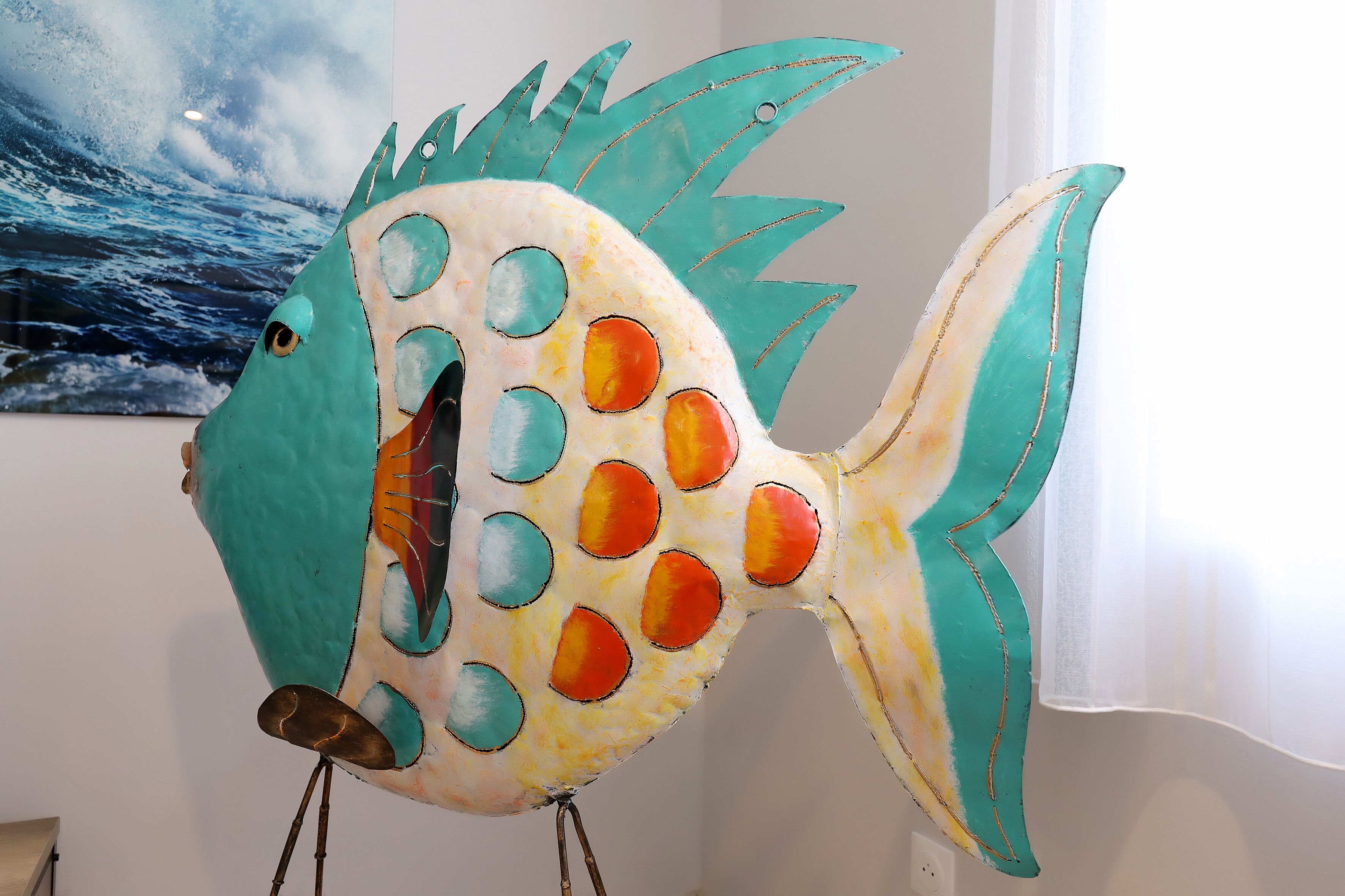 A colorful fish sculpture with a teal and yellow body, orange spots, and a blue tail.