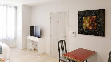 Een kamer met een bed, een bureau met een televisie, een eettafel met stoelen en een muur met een geometrisch kunstwerk.