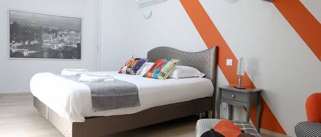 Un dormitorio moderno con una cama grande, vista a la ciudad, una pared de acento gris y naranja, y una mesita de noche pequeña.