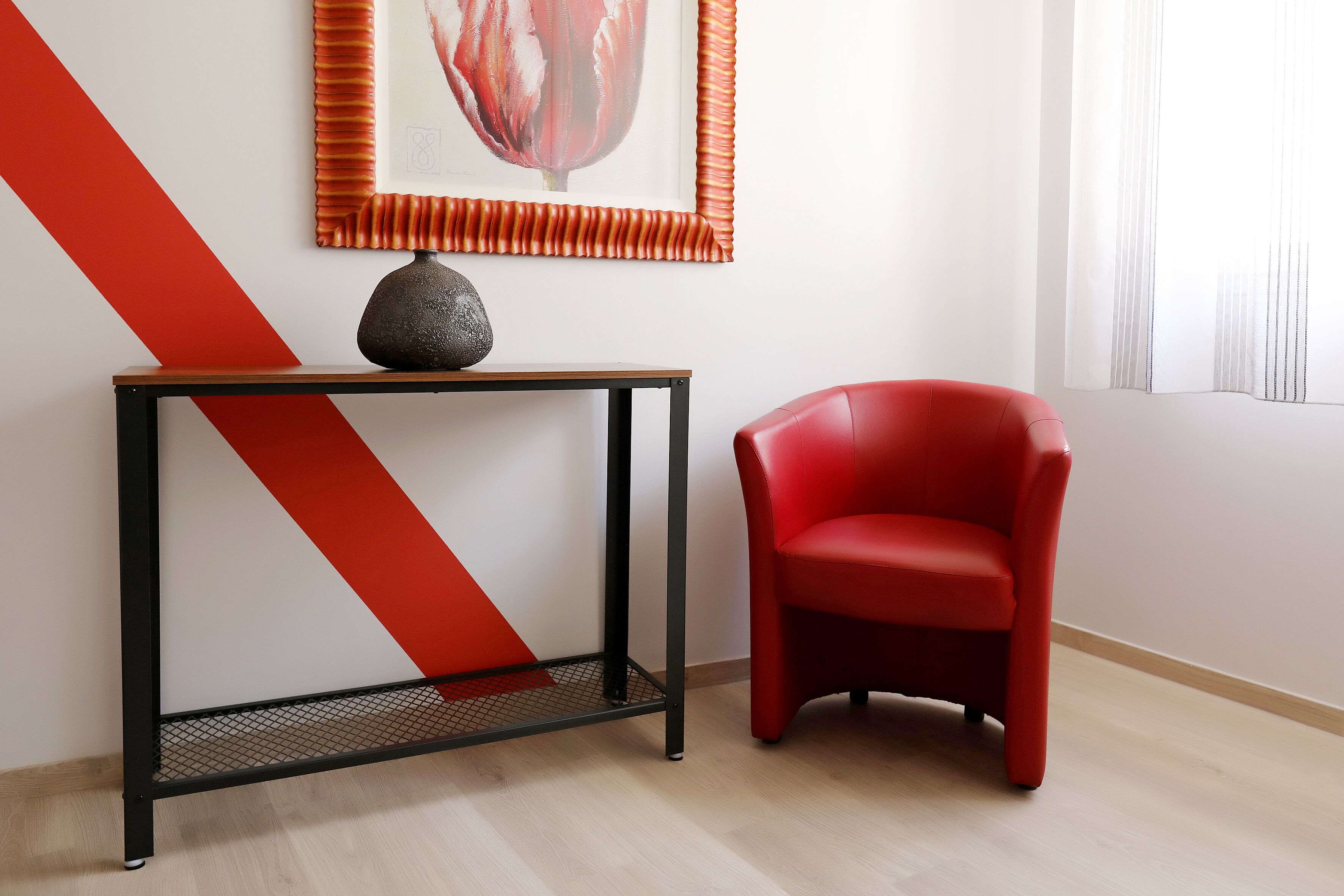 A modern room with a red chair, a black metal console table, and a framed artwork on the wall.