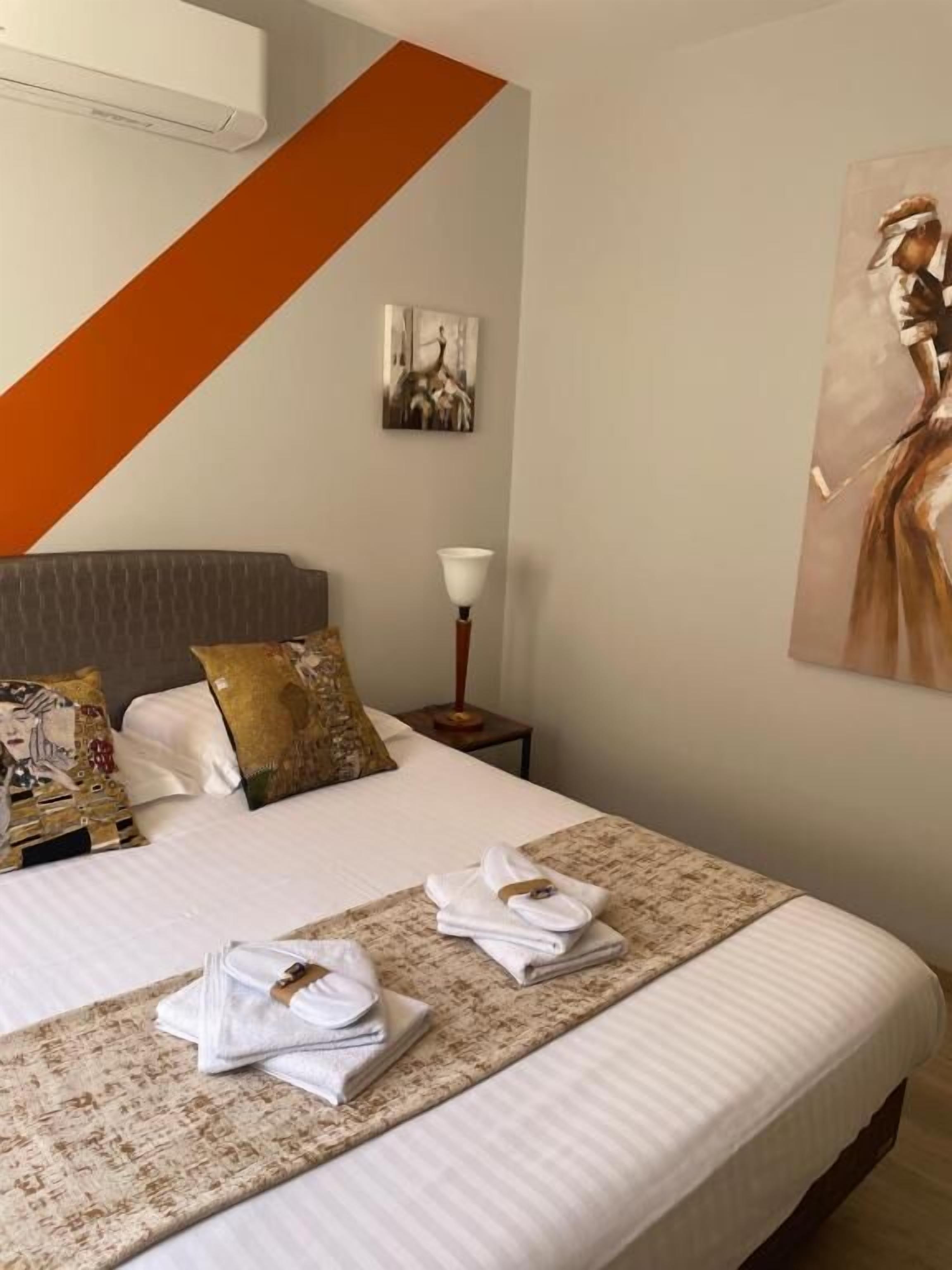 Una cama bien tendida con almohadas, una lámpara de noche y un cuadro en la pared.