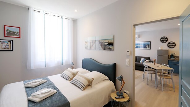 A modern hotel room with a neatly made bed, a small round table with a lamp, and a view of the adjacent living area. - Le Porta 5 (Albi)