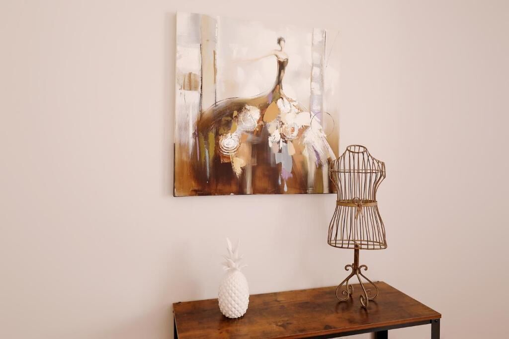 A room with a wooden table, a pineapple decoration, a metal birdcage, and a large abstract painting on the wall.