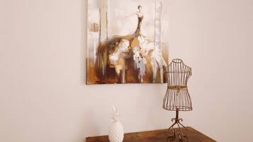 A room with a wooden table, a pineapple decoration, a metal birdcage, and a large abstract painting on the wall.