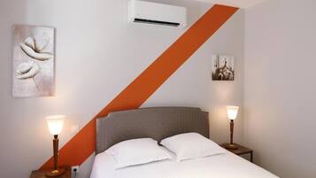 A hotel room with a bed, two bedside tables with lamps, an air conditioning unit, and artwork on the walls.