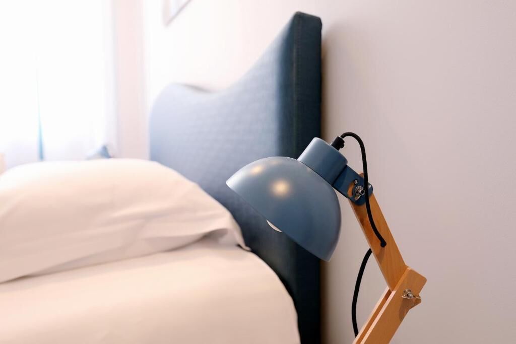 A bed with white linens and a blue headboard, a wooden bedside table, and a blue desk lamp with a flexible arm.